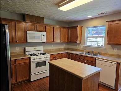 Kitchen with white appliances, dark wood-style flooring, brown cabinetry, and light countertops