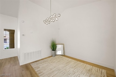 Unfurnished room featuring lofted ceiling, wood finished floors, and a chandelier