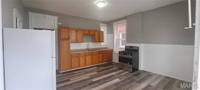 Kitchen featuring freestanding refrigerator, light countertops, stainless steel range with gas stovetop, and dark wood-type flooring