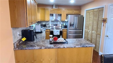 Kitchen with tasteful backsplash, appliances with stainless steel finishes, wall chimney exhaust hood, and dark wood-style flooring