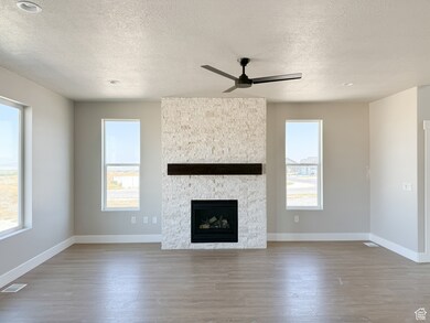 Unfurnished living room with a stone fireplace, light wood finished floors, a textured ceiling, and ceiling fan