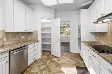 Kitchen with backsplash, white cabinets, stainless steel appliances, a chandelier, and dark stone countertops