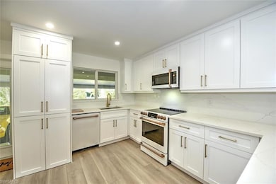 Kitchen featuring white appliances, a sink, white cabinetry, light wood-type flooring, and recessed lighting