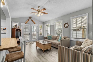 Living area featuring french doors, light wood finished floors, ceiling fan, a textured ceiling, and lofted ceiling