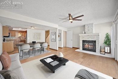 Living room featuring light wood-type flooring, a fireplace, a textured ceiling, and a ceiling fan. This is a virtually staged photo.