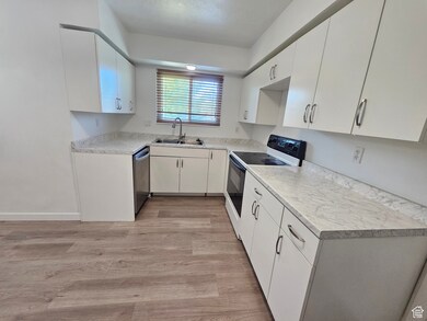 Kitchen featuring white electric stove, light countertops, light wood-style flooring, white cabinets, and stainless steel dishwasher
