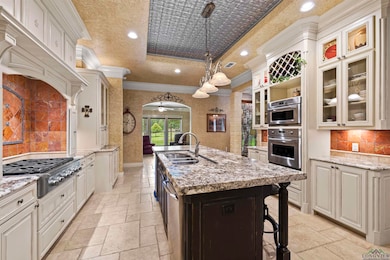 Kitchen featuring stone tile flooring, ornamental molding, a raised ceiling, appliances with stainless steel finishes, and an island with sink