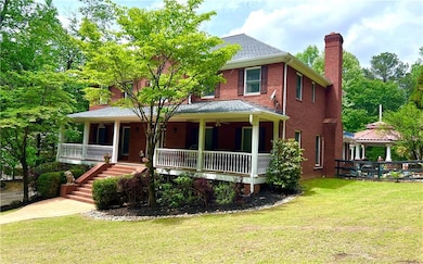 View of front facade featuring a chimney, covered porch, brick siding, a gazebo, and a front lawn