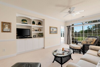 Living area with built in shelves, ceiling fan, a textured ceiling, crown molding, and light colored carpet