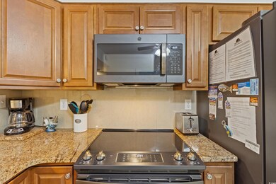 Kitchen featuring appliances with stainless steel finishes, brown cabinetry, light stone counters, and a toaster