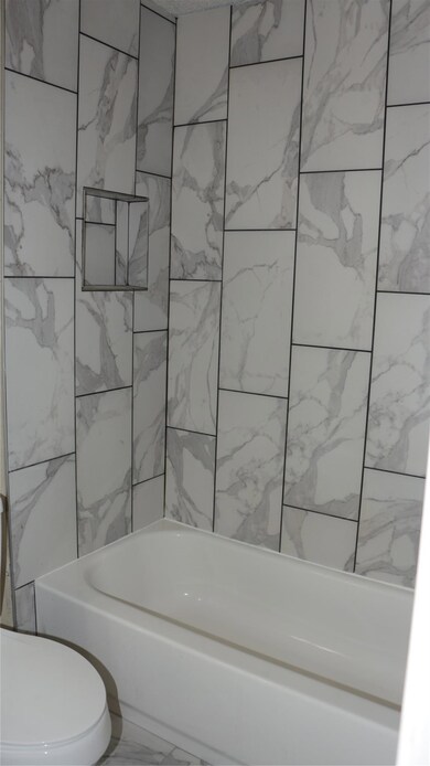 Bathroom with marble look tiles and tub / shower 