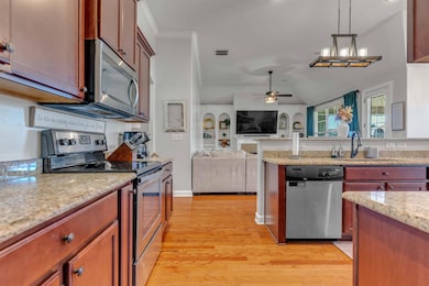 Kitchen with appliances with stainless steel finishes, light stone countertops, open floor plan, light wood finished floors, and decorative light fixtures