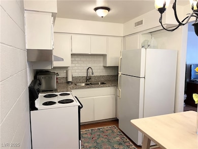 Kitchen with white appliances, visible vents, decorative backsplash, white cabinetry, and a sink