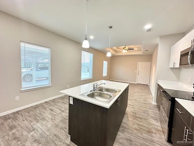 Kitchen featuring black electric range, a tray ceiling, light countertops, pendant lighting, and a center island with sink