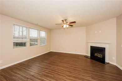 Unfurnished living room featuring a ceiling fan, dark wood-type flooring, a fireplace with raised hearth, and baseboards