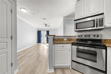 Kitchen featuring appliances with stainless steel finishes, white cabinets, a textured ceiling, a peninsula, and backsplash