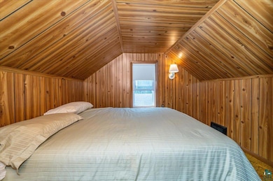 Carpeted bedroom with wooden walls, vaulted ceiling, and wooden ceiling