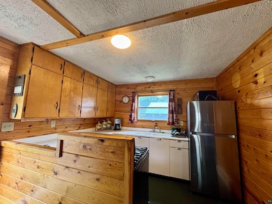 Kitchen with freestanding refrigerator, wooden walls, light countertops, a sink, and black range with gas stovetop