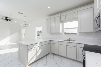 Kitchen featuring decorative backsplash, visible vents, a peninsula, stainless steel microwave, and a sink