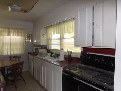 The kitchen has a large electric stove and a sink with double windows. 