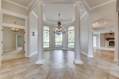 Foyer with a chandelier, ornamental molding, ornate columns, and light tile patterned floors