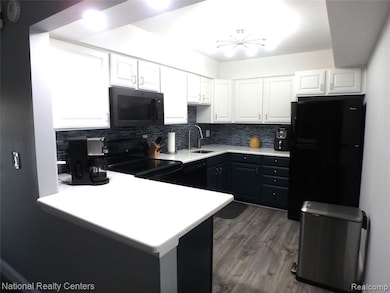 Kitchen featuring tasteful backsplash, white cabinets, black appliances, light countertops, and a peninsula