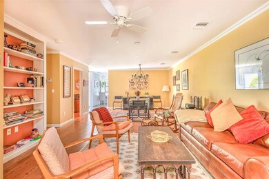 Living room with crown molding, light wood-style flooring, ceiling fan, baseboards, and a chandelier