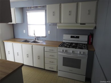 Kitchen with white range with gas cooktop, wood counters, light tile patterned flooring, and white cabinetry