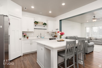 Kitchen featuring a kitchen bar, open floor plan, freestanding refrigerator, dark wood-style floors, and white cabinets