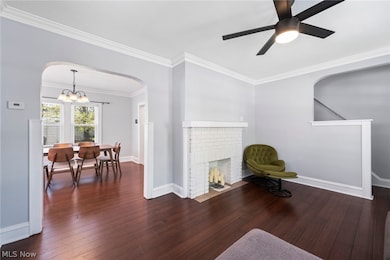 Sitting room with ornamental molding, dark hardwood / wood-style flooring, ceiling fan with notable chandelier, and a brick fireplace
