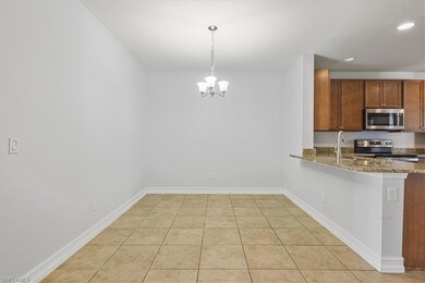 Kitchen featuring stainless steel appliances, a chandelier, stone counters, brown cabinets, and decorative light fixtures