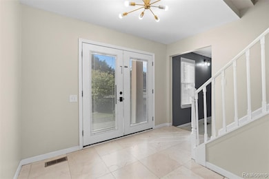Foyer featuring stairway, a chandelier, french doors, and light tile patterned flooring