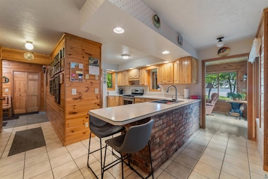 Kitchen with stainless steel gas stove, light tile patterned flooring, wooden walls, light countertops, and a peninsula