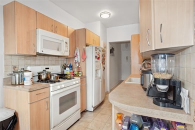 Kitchen featuring light tile patterned flooring, a sink, white appliances, light countertops, and backsplash