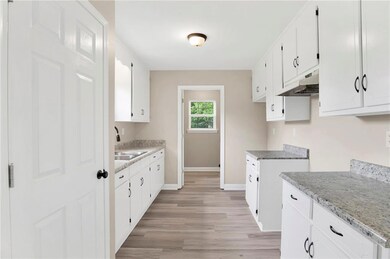 Kitchen featuring a sink, under cabinet range hood, baseboards, light wood finished floors, and white cabinets