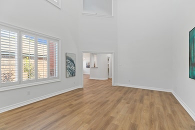 View of the GRAND two-story living room filled with natural light from Pella windows framed by Plantation Shutters leading to the dining area.