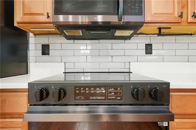 Kitchen view of stainless steel microwave, electric range oven, tasteful backsplash, and light countertops