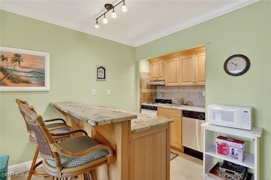 Kitchen with tasteful backsplash, light brown cabinets, white appliances, ornamental molding, and light stone counters