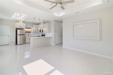 Kitchen with appliances with stainless steel finishes, a tray ceiling, a ceiling fan, a sink, and baseboards