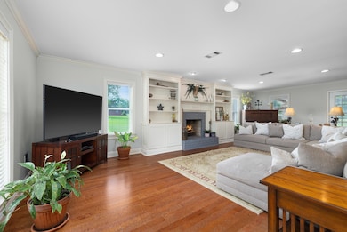 Living area with wood finished floors, crown molding, recessed lighting, a brick fireplace, and baseboards