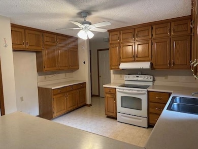 Kitchen with electric range, under cabinet range hood, brown cabinetry, and a textured ceiling