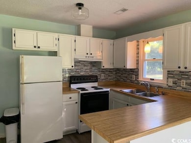 Kitchen with freestanding refrigerator, electric stove, white cabinetry, backsplash, and light countertops