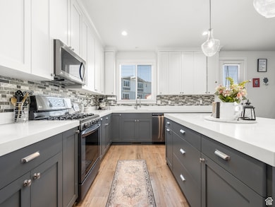 Kitchen featuring white cabinetry, tasteful backsplash, appliances with stainless steel finishes, and decorative light fixtures