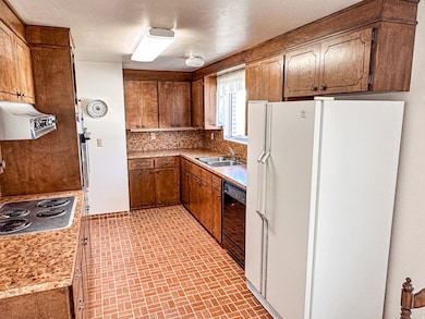 Kitchen featuring freestanding refrigerator, light countertops, brown cabinets, stainless steel electric cooktop, and brick patterned flooring