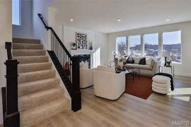 Living room with healthy amount of natural light, light wood-type flooring, stairs, recessed lighting, and a glass covered fireplace