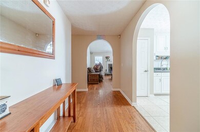 Hallway featuring arched walkways, light wood-style flooring, a textured ceiling, a sink, and baseboards