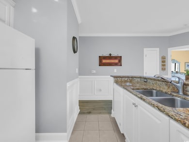 Kitchen featuring dark stone counters, white cabinetry, wainscoting, white appliances, and ornamental molding