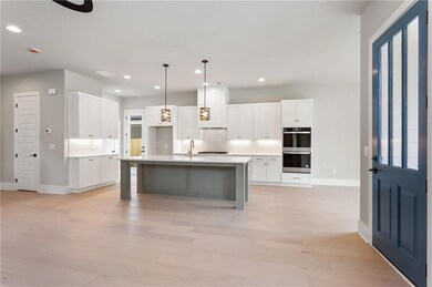 Kitchen with recessed lighting, light wood-type flooring, tasteful backsplash, white cabinets, and an island with sink