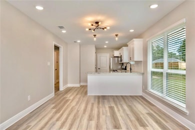 Images are of a model home and may include custom design features not available in other homes. Kitchen featuring white cabinets, a chandelier, light stone countertops, a peninsula, and light wood finished floors