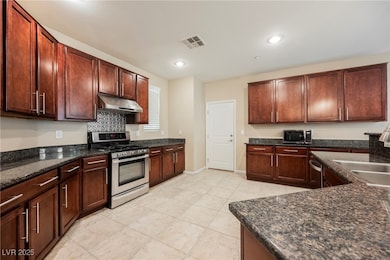 Kitchen with appliances with stainless steel finishes, dark stone countertops, under cabinet range hood, tasteful backsplash, and light tile patterned flooring